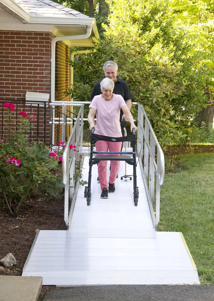 Senior woman using walker on white aluminum wheelchair ramp with safety handrails
