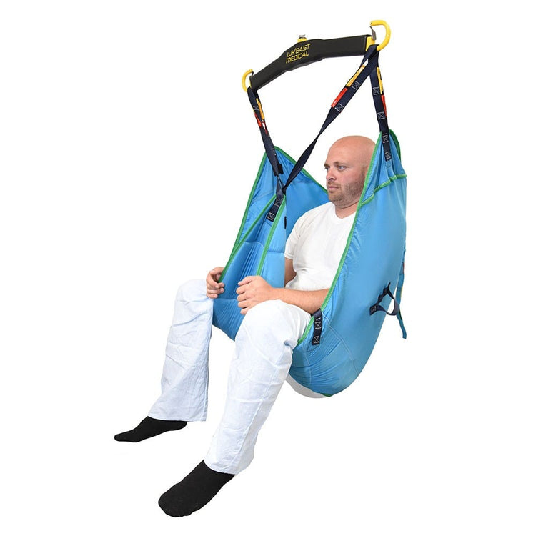 Man sitting in a full-body patient lift sling attached to a medical lift system, wearing white clothing and black socks, demonstrating safe patient transfer equipment for mobility support.