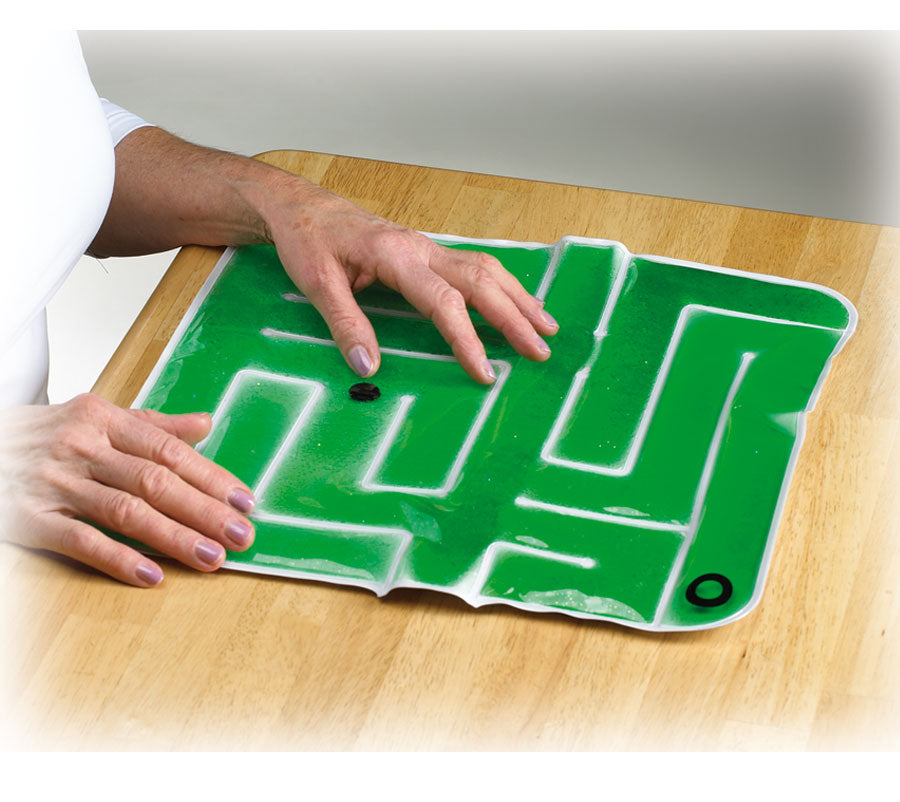 Person playing with a maze game on a green mat with white lines on a wooden table.