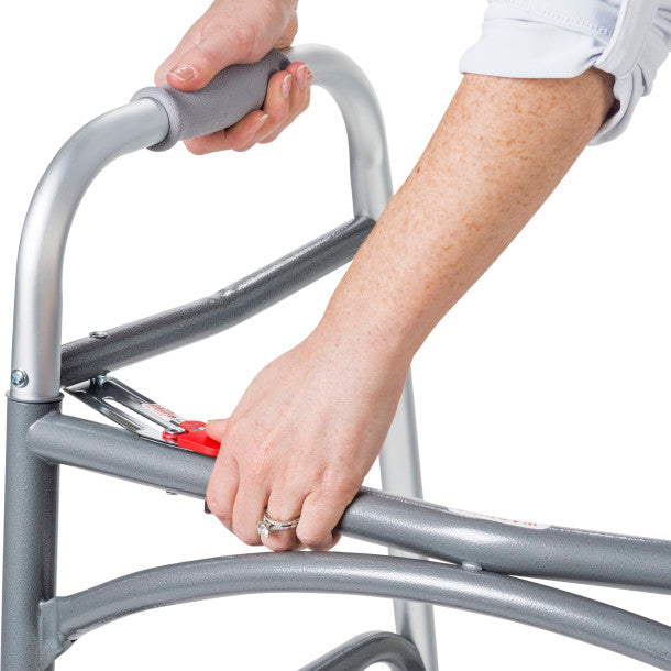 Person using a silver walker with red handle on a white background