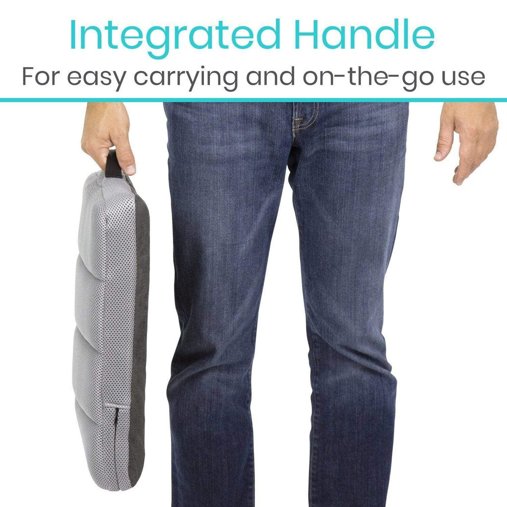 Person holding a gray travel pillow with an integrated handle, wearing blue jeans on a white background.