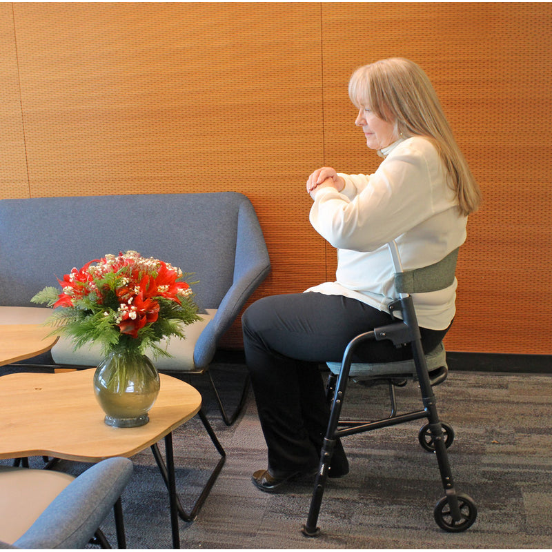 Woman using a walker in a waiting room with a vase of flowers on a table.