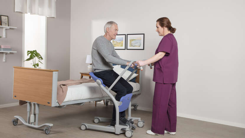 Person using a patient lift with a healthcare professional assisting them.