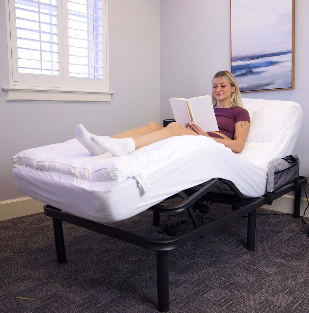 Woman reading a book on a adjustable bed in a room with a window and painting.