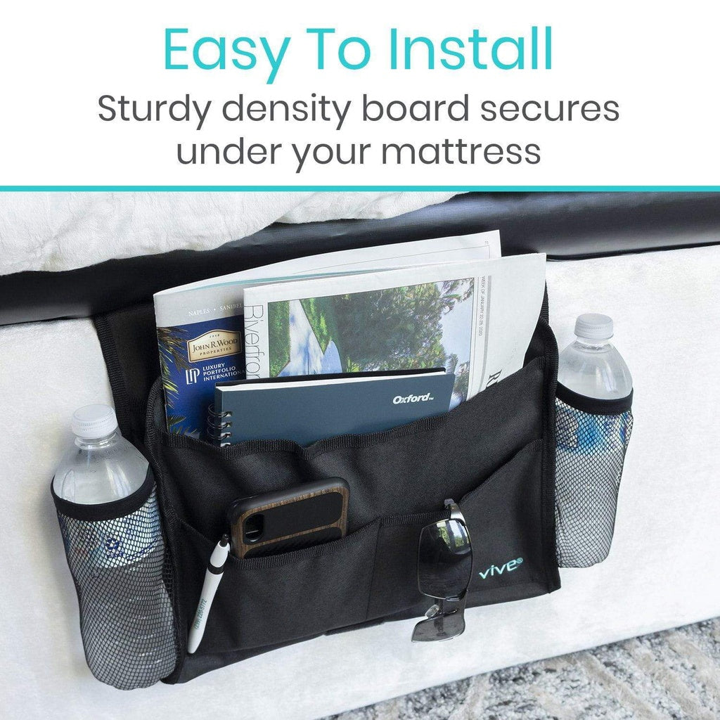 Black bed caddy with multiple compartments holding books, bottles, and a phone on a bed.