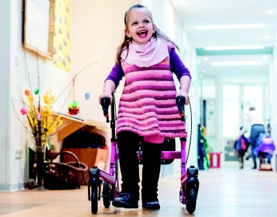 Child in a pink dress using a walker in an indoor setting
