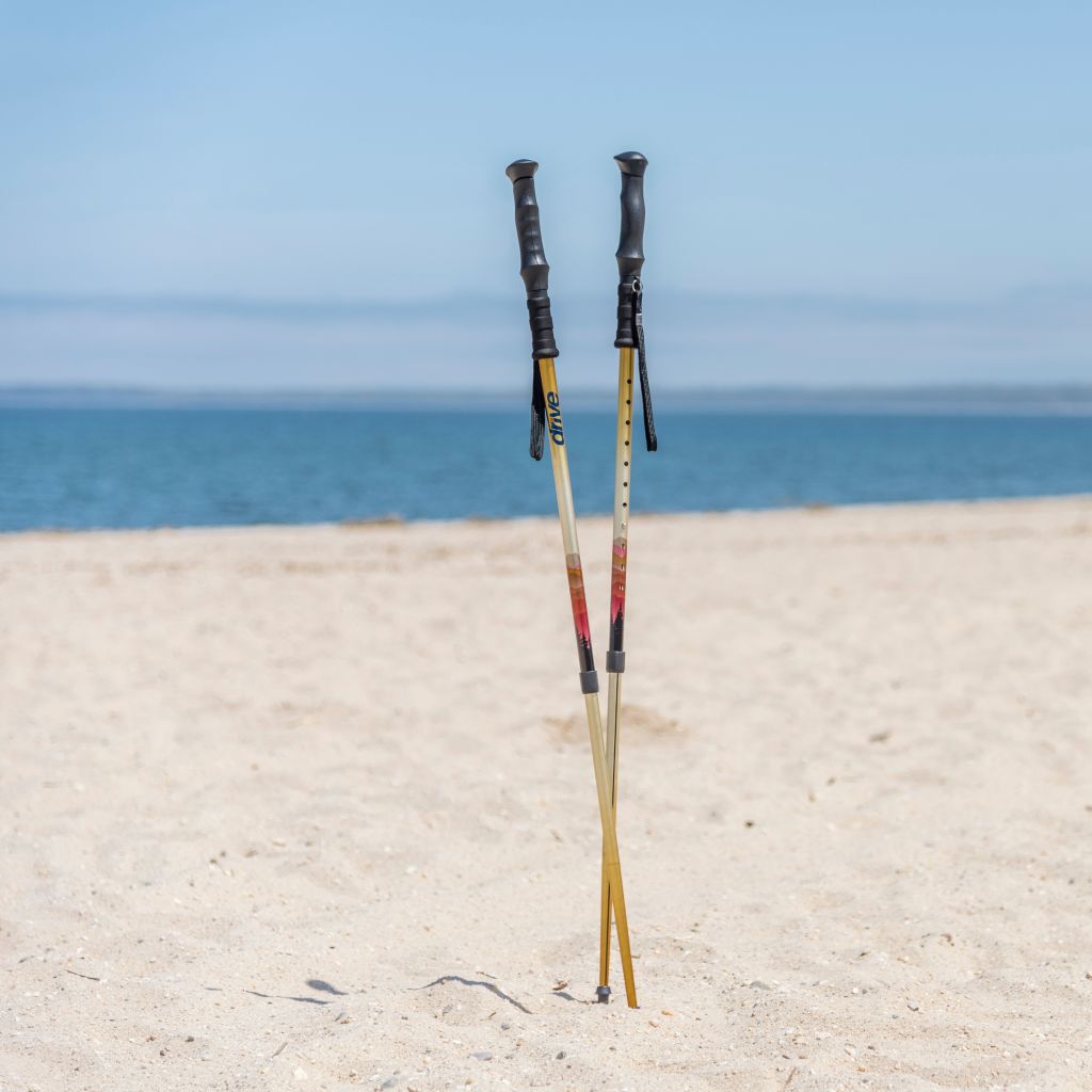 Two hiking poles standing on a sandy beach with ocean and clear sky in the background.