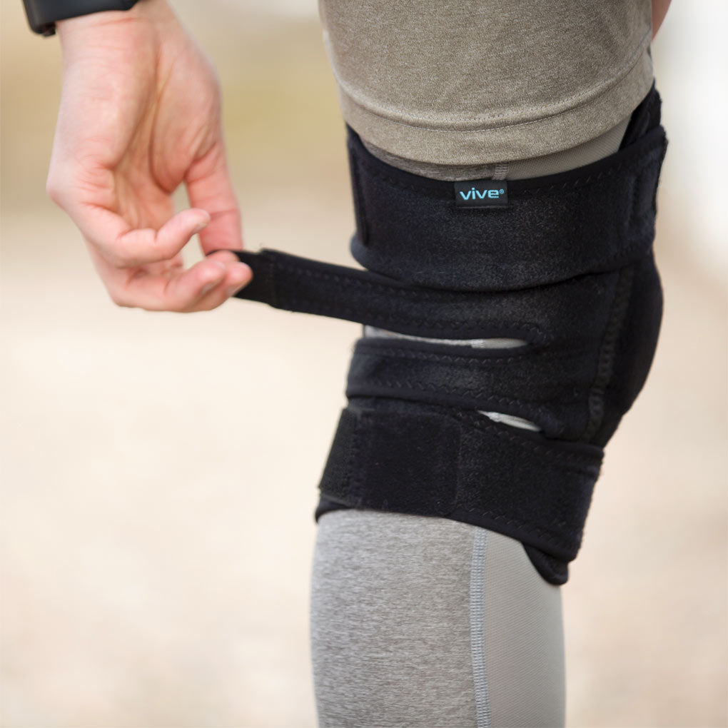 Person wearing a black knee brace with 'vive' branding on a beige background