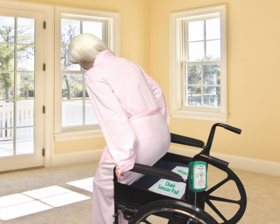 Person in a pink outfit with a wheelchair featuring a sensor pad in a room with yellow walls and large windows.