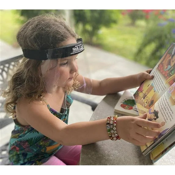 Child reading a book outdoors with a headband and colorful bracelets.