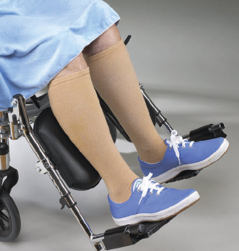 Person in a wheelchair wearing blue shoes and beige compression stockings.