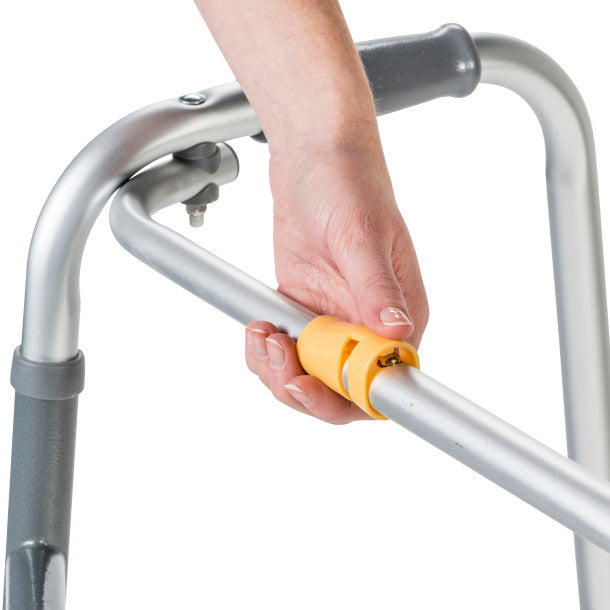 Hand holding a yellow handle on a silver walker against a white background