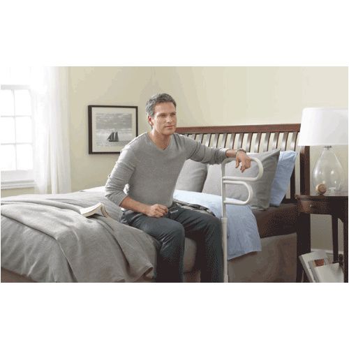 Man sitting on a bed using a hospital rail in a bedroom setting.