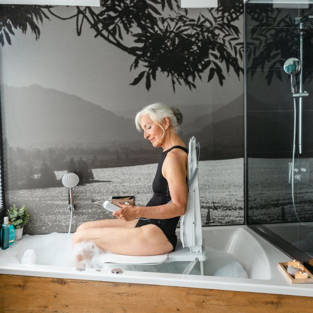Woman using a smartphone in a bathtub with a scenic wall mural.