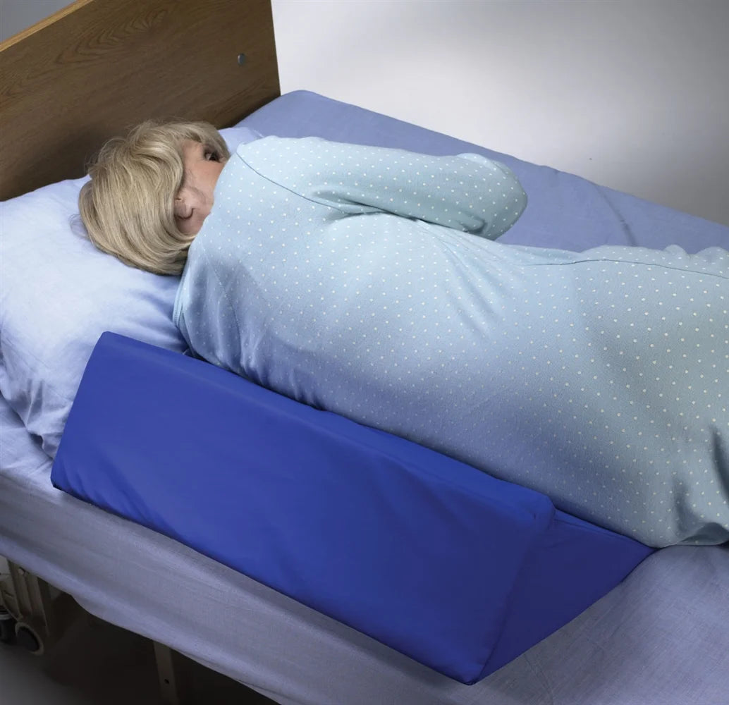 Person lying in bed with a blue wedge pillow under their knees