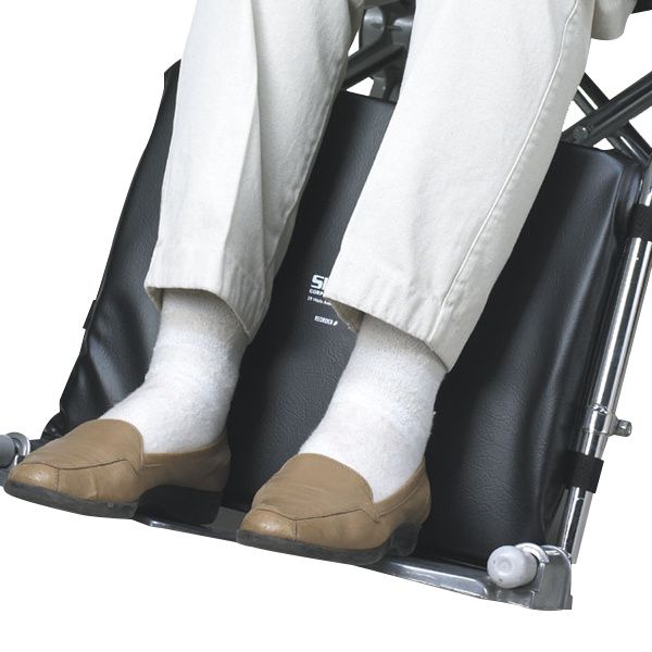 Person sitting on a black footstool with white pants and brown shoes.