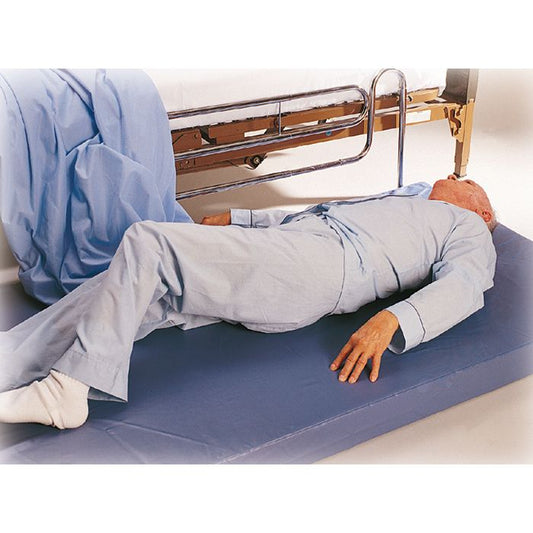 Person lying on a blue mat with a hospital bed in the background