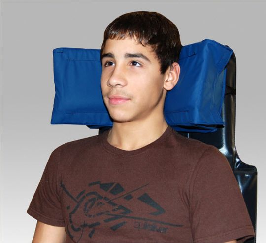Person wearing a brown t-shirt with a graphic design, standing in front of a gray background with blue bags on shoulders.