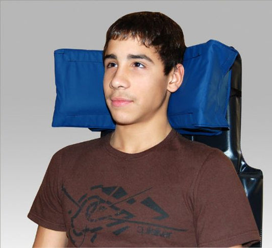 Person wearing a brown t-shirt with a graphic design, standing in front of a gray background with blue bags on shoulders.