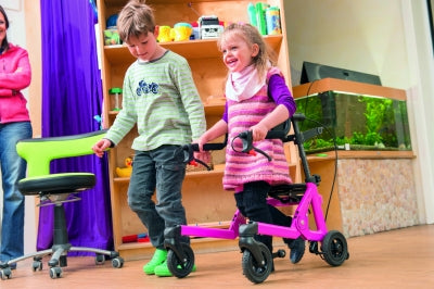 Two children playing with a scooter in a room with a bookshelf and aquarium.