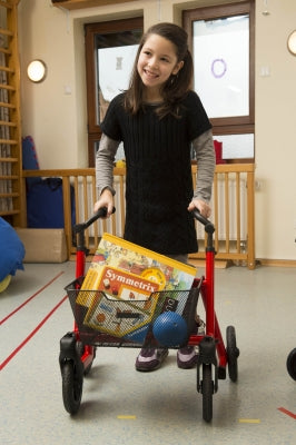 Child pushing a cart with supplies in a classroom setting