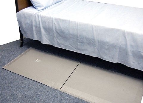 grey bed mat on the floor next to a bed with white sheets.