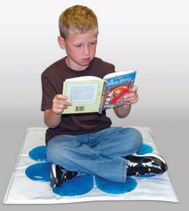 Child sitting on a blue and white mat reading a book against a plain background