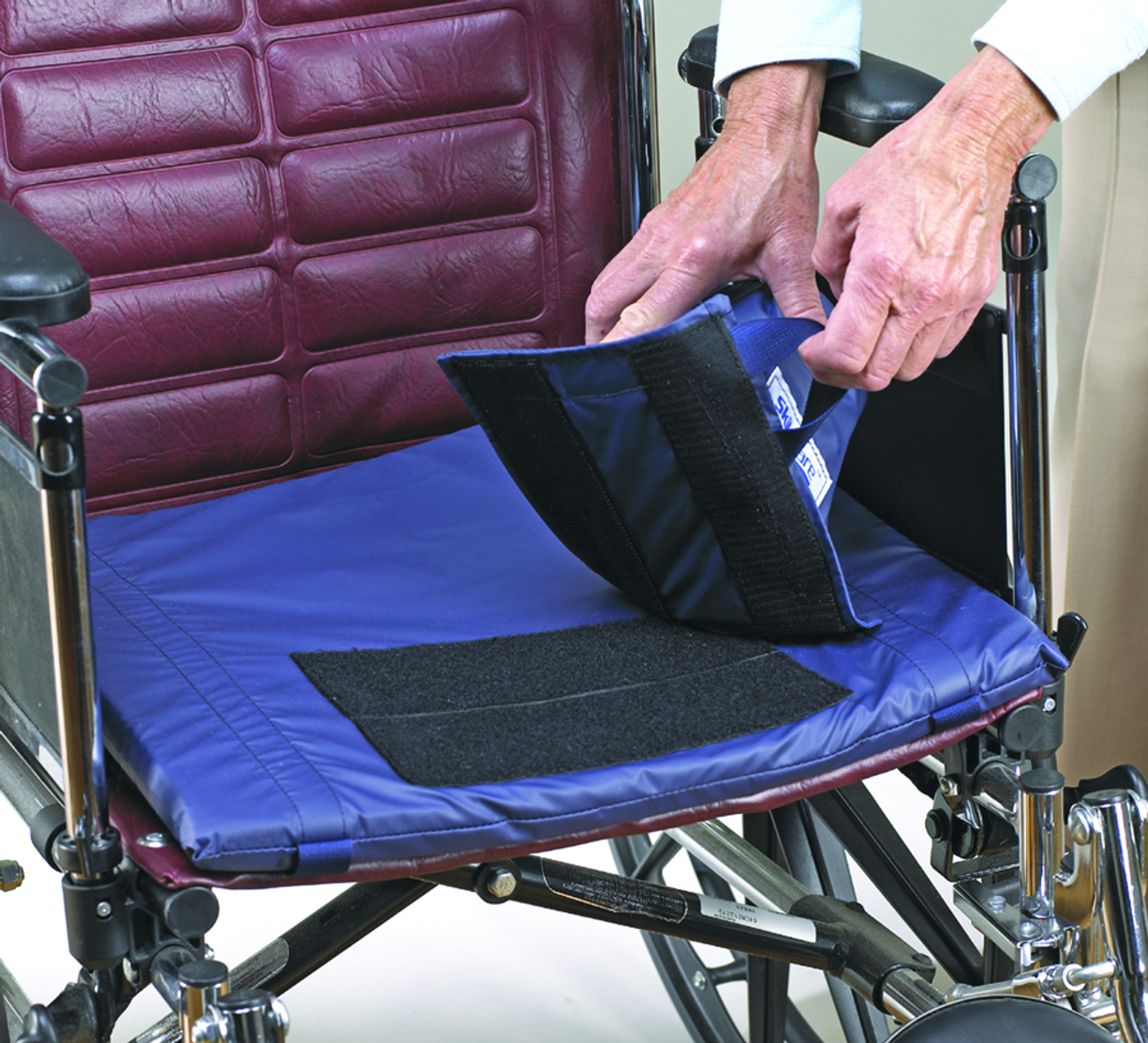 Person adjusting a blue wheelchair cushion on a maroon wheelchair.