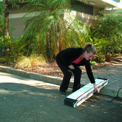 Person carrying a folded mat on a sidewalk with greenery in the background
