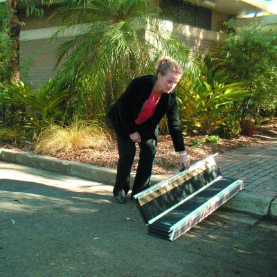 Person in a black suit and red shirt bending over a large box outdoors with greenery in the background