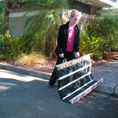 Person carrying a large black and white product on a sidewalk with greenery in the background