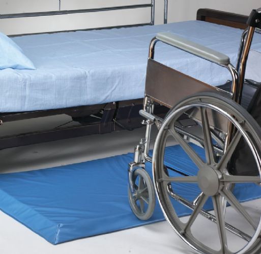 Wheelchair next to a hospital bed with blue mattress on a white floor.