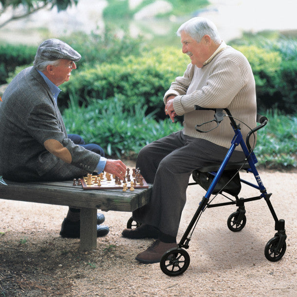 Two elderly men playing chess outdoors, one using a walker.
