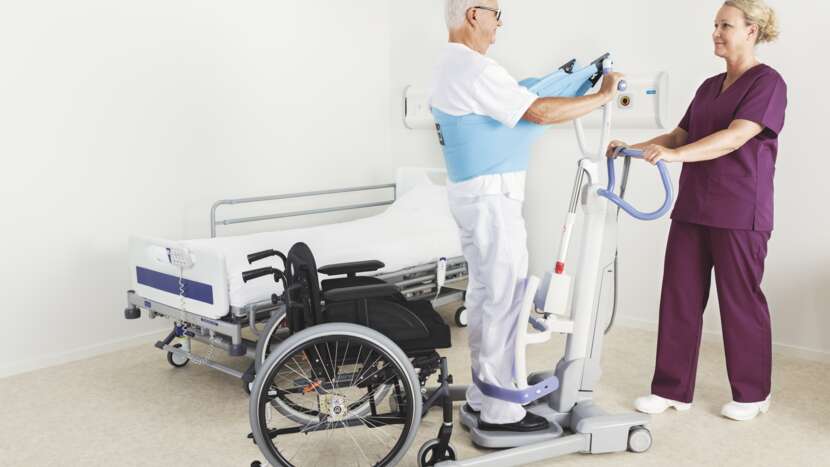 Two healthcare professionals using a patient lift to assist a person in a wheelchair.