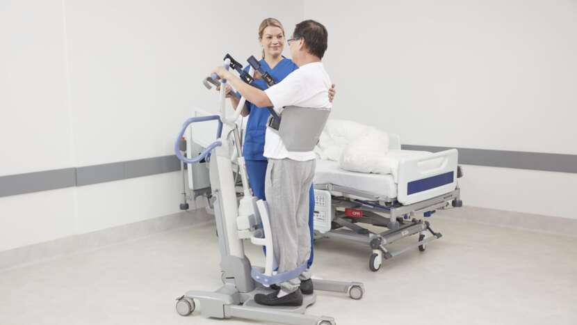 Person using a hospital lift with another person assisting in a clinical setting