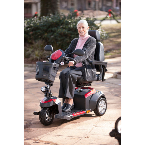 Woman using a mobility scooter outdoors on a paved path.