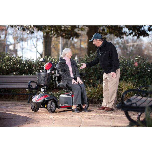 Man assisting an elderly woman with a mobility scooter in a park setting.