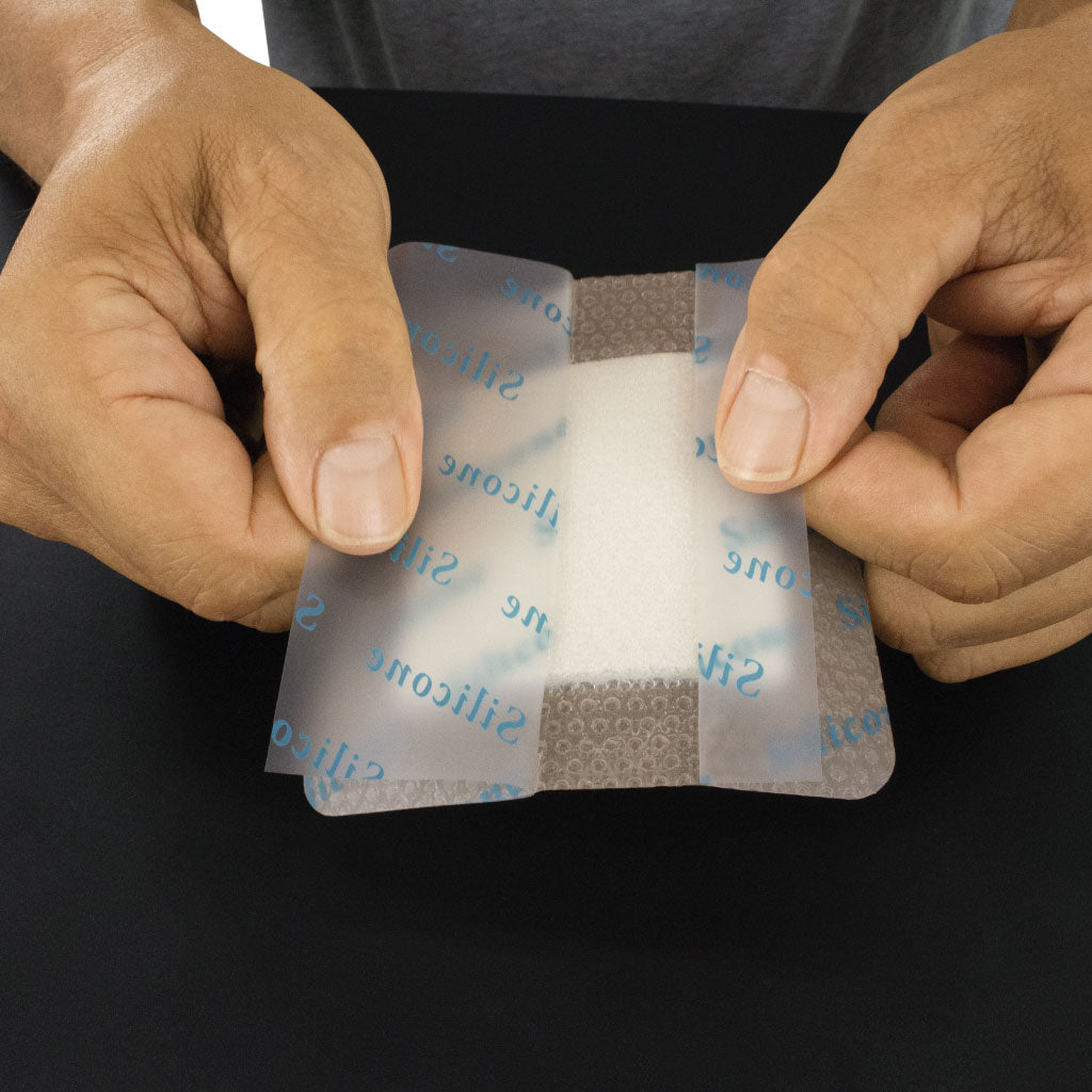 Hands holding a small medical patch with silicone adhesive on a black background