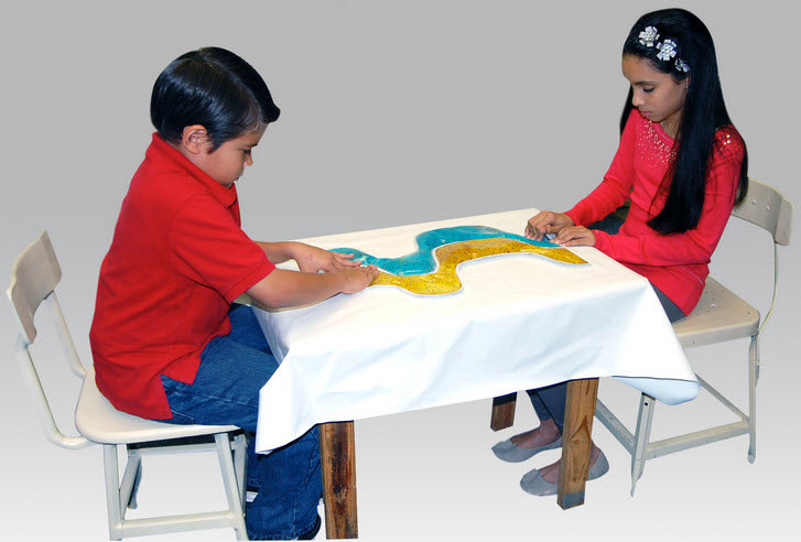 Two children sitting at a table with a colorful sand tray game on a plain background