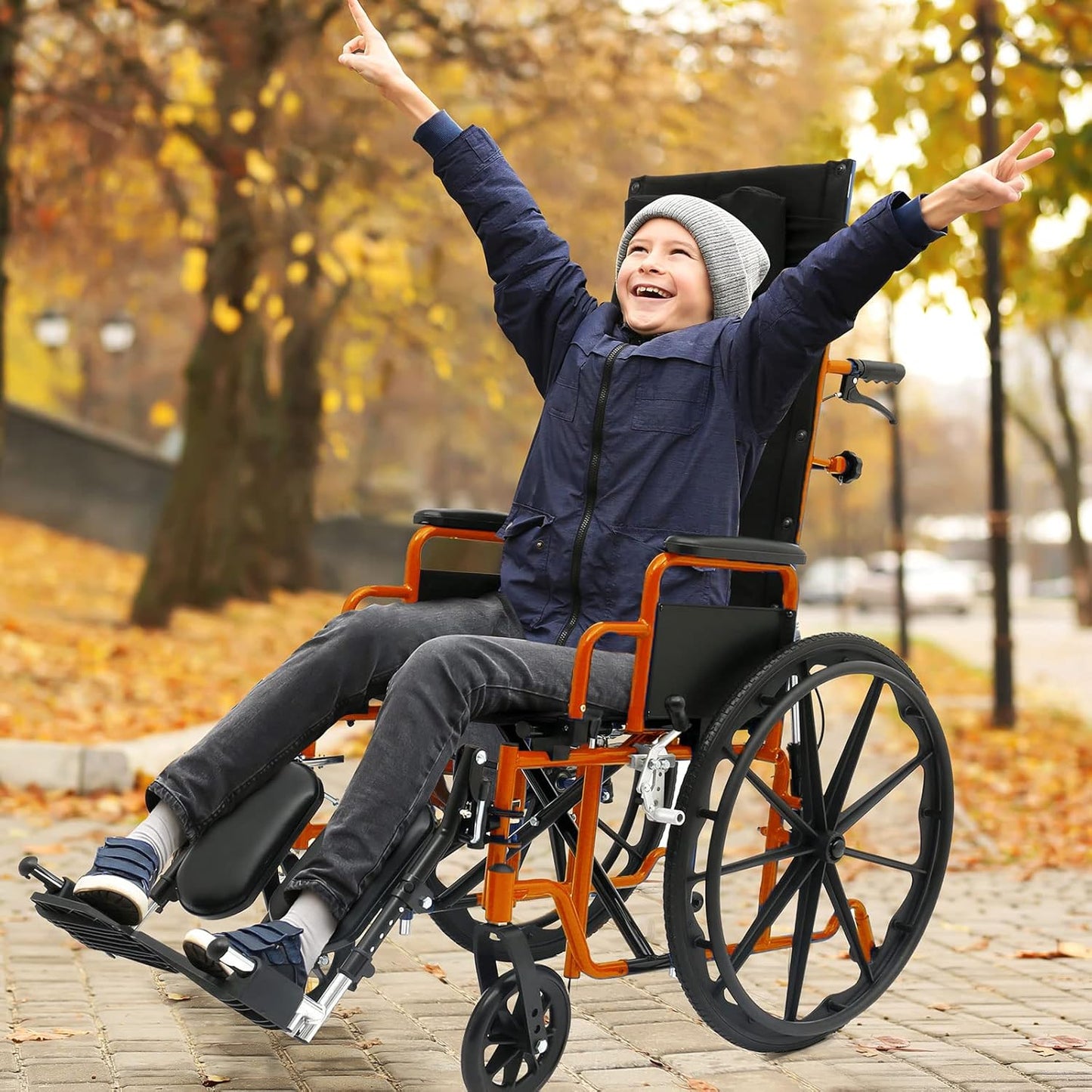 Child in a wheelchair with arms raised in an autumn park