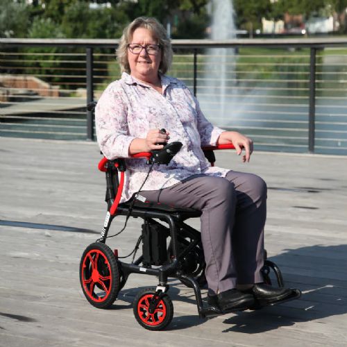 Person using a mobility scooter outdoors on a wooden deck with greenery in the background