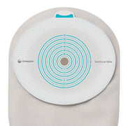 A Coloplast SenSura Mia circular monitoring pad with a white textured surface, teal concentric rings, and a central hole, shown on a beige fabric backing against a white background.
