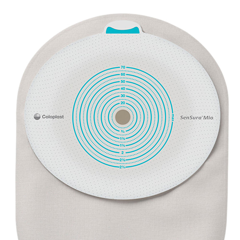 A Coloplast SenSura Mia circular monitoring pad with a white textured surface, teal concentric rings, and a central hole, shown on a beige fabric backing against a white background.