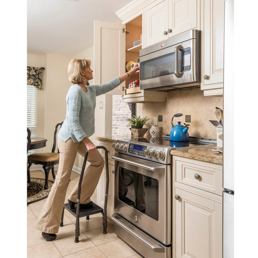 Woman using a step stool to reach a high cabinet in a kitchen.