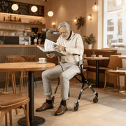 Man with a walker reading a newspaper in a cafe.