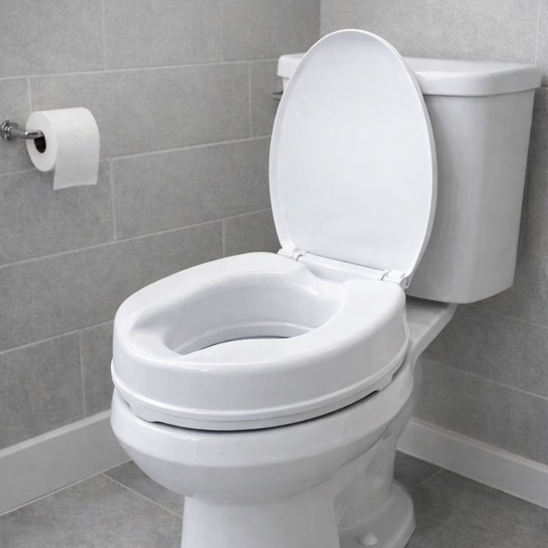 A white ceramic toilet with the lid open, set in a tiled bathroom with gray wall and floor tiles. A roll of toilet paper is mounted on the left wall.