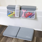 A gray foldable bath mat with white trim and the HeartiGart logo is shown on a wooden floor in front of a white bathtub. Above the tub, a matching gray mesh hanging organizer pocket holds bath toys and a bottle, demonstrating its use in a bathroom setting.