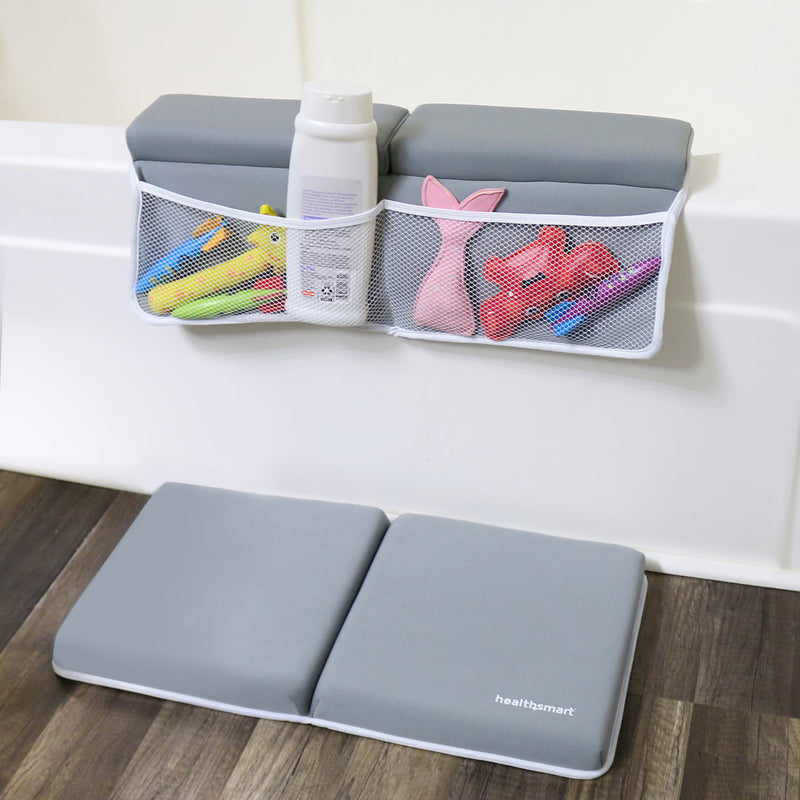 A gray foldable bath mat with white trim and the HeartiGart logo is shown on a wooden floor in front of a white bathtub. Above the tub, a matching gray mesh hanging organizer pocket holds bath toys and a bottle, demonstrating its use in a bathroom setting.