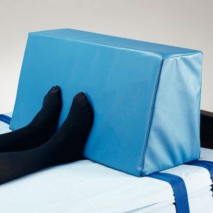 Blue foam wedge used as a footrest on a bed with black socks.
