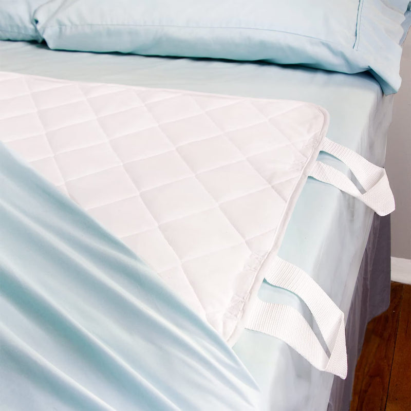 A white quilted mattress protector with two white carrying straps, shown draped over a bed with light blue bedding.